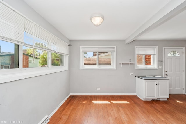 unfurnished dining area featuring plenty of natural light, light wood finished floors, baseboards, and beamed ceiling