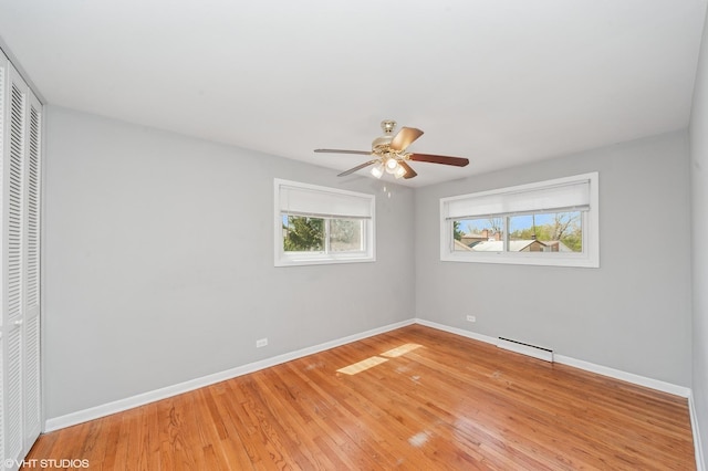 unfurnished bedroom with a baseboard heating unit, a closet, baseboards, light wood-type flooring, and a ceiling fan