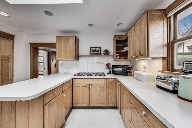 kitchen featuring a peninsula, backsplash, stainless steel gas stovetop, open shelves, and light countertops