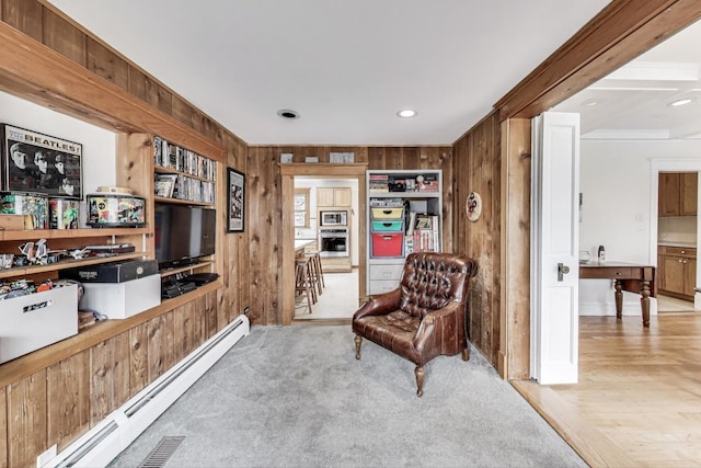 sitting room with a baseboard heating unit, light carpet, and wooden walls