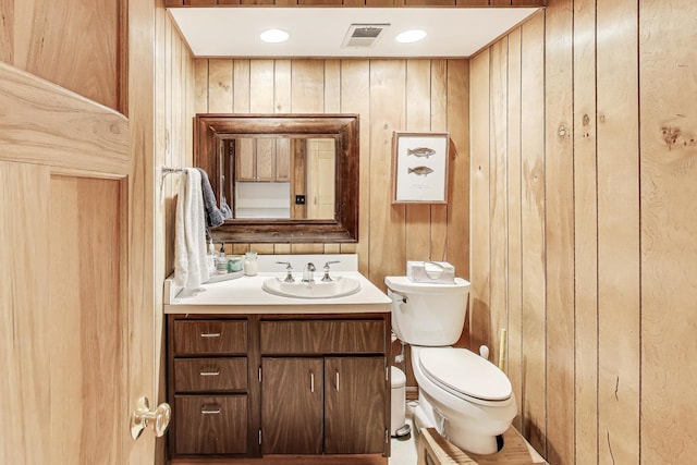bathroom featuring toilet, vanity, and wood walls