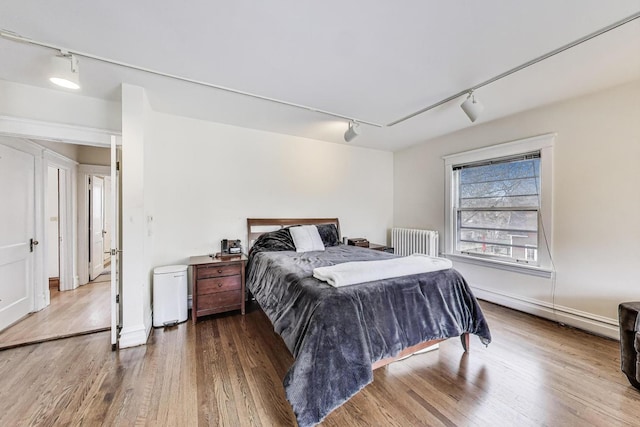 bedroom with wood finished floors, rail lighting, and radiator