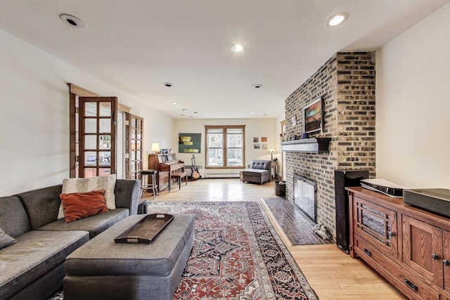 living room with light wood-type flooring, a fireplace, recessed lighting, and a baseboard heating unit