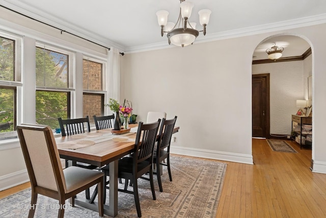 dining space featuring arched walkways, ornamental molding, light wood-style flooring, and a chandelier