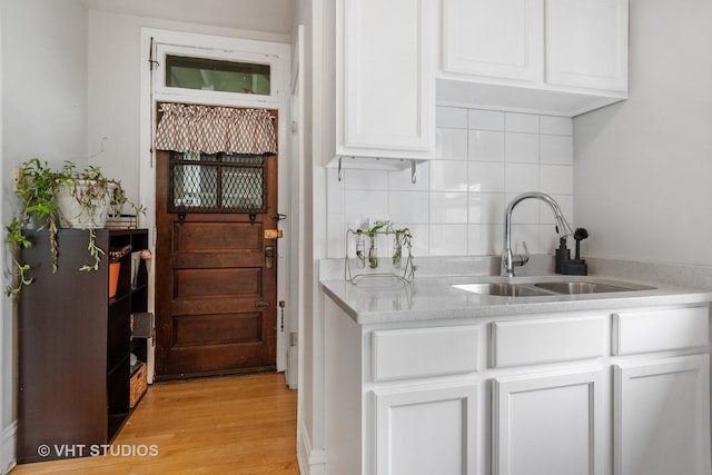 kitchen with backsplash, a sink, light countertops, light wood-style floors, and white cabinetry