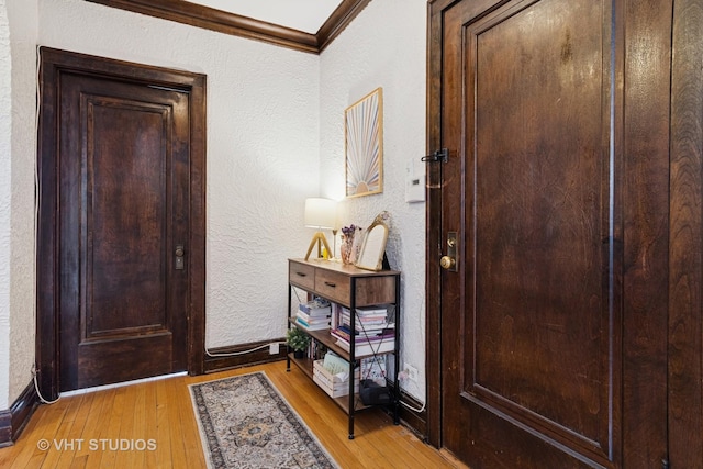 foyer featuring light wood-style floors, baseboards, a textured wall, and ornamental molding