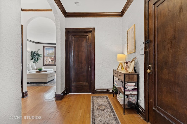 entrance foyer featuring crown molding, arched walkways, a textured wall, and light wood-type flooring