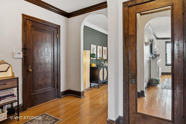 entrance foyer featuring arched walkways, ornamental molding, a textured wall, and light wood-style flooring