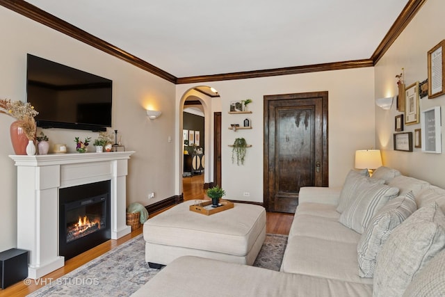 living room featuring arched walkways, wood finished floors, baseboards, a glass covered fireplace, and ornamental molding