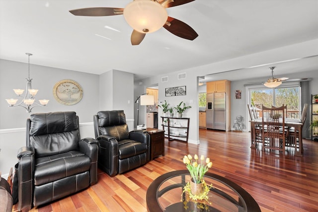 living area with visible vents, ceiling fan with notable chandelier, and light wood-type flooring
