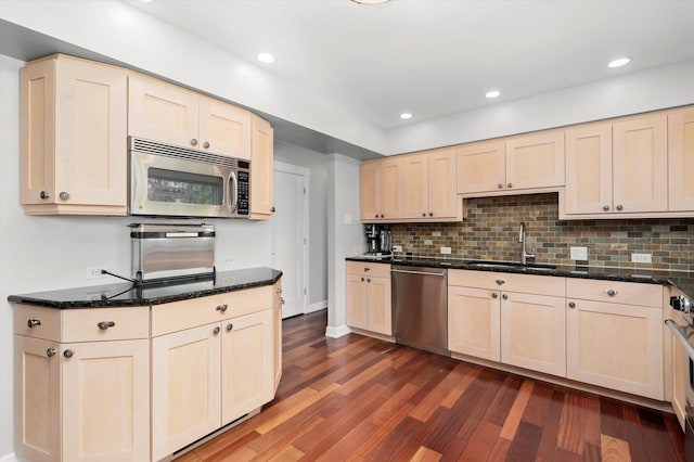 kitchen with light brown cabinetry, appliances with stainless steel finishes, a sink, decorative backsplash, and dark wood-type flooring