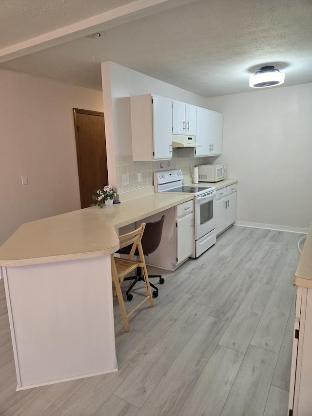 kitchen featuring light wood finished floors, under cabinet range hood, light countertops, white appliances, and a peninsula