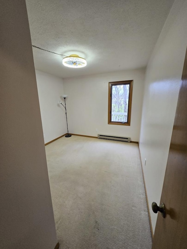 empty room with a baseboard heating unit, baseboards, a textured ceiling, and light colored carpet