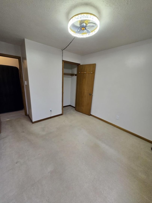 unfurnished bedroom with a textured ceiling, a closet, baseboards, and light carpet