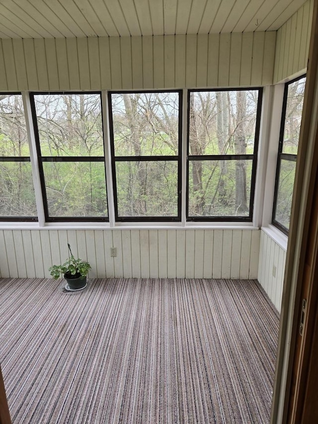 unfurnished sunroom with carpet floors, wood walls, and a wealth of natural light