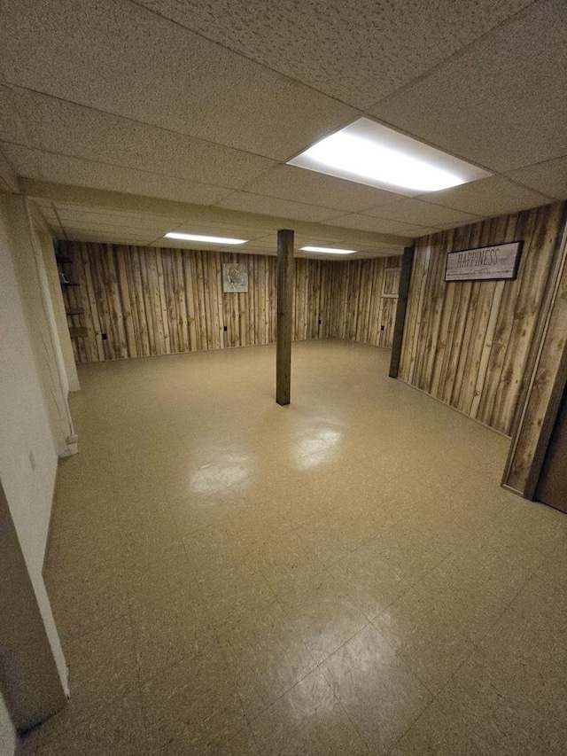 finished below grade area with a paneled ceiling, tile patterned floors, and wood walls