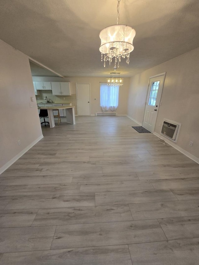 unfurnished dining area with a chandelier, light wood finished floors, baseboards, and heating unit