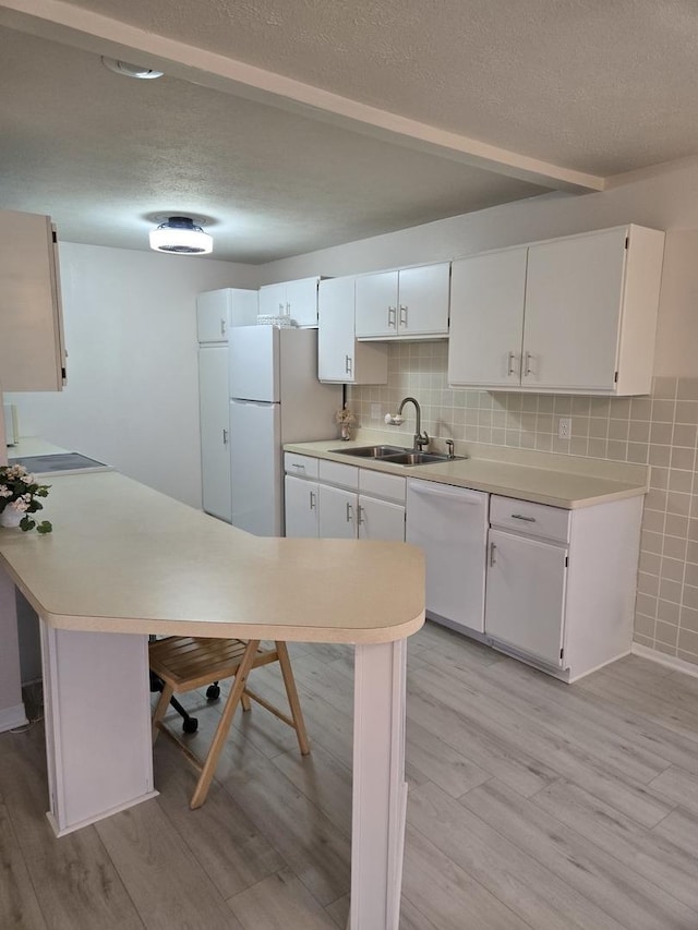 kitchen featuring white appliances, a textured ceiling, light wood finished floors, and a sink