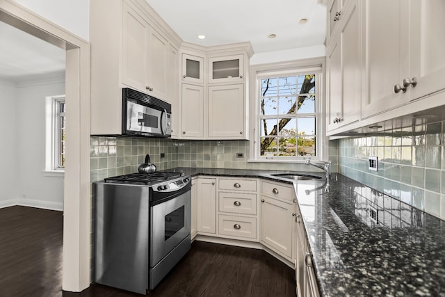 kitchen featuring appliances with stainless steel finishes, a sink, dark wood finished floors, dark stone countertops, and recessed lighting