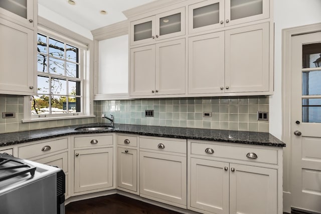 kitchen featuring a sink, range, backsplash, glass insert cabinets, and dark stone countertops