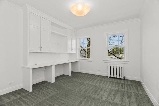 unfurnished office featuring radiator heating unit, dark carpet, baseboards, crown molding, and built in desk