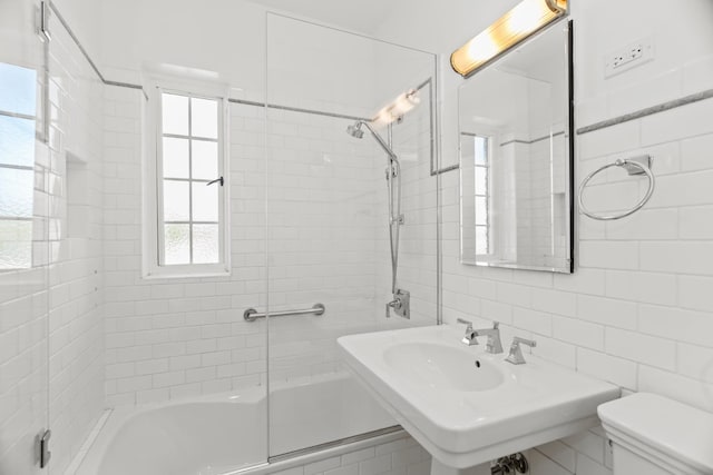 bathroom with tile walls, toilet,  shower combination, and a sink