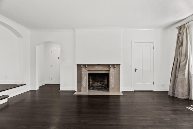 unfurnished living room with dark wood-style floors, ornamental molding, arched walkways, a high end fireplace, and baseboards