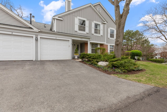 view of front of property featuring a chimney, board and batten siding, asphalt driveway, brick siding, and a garage