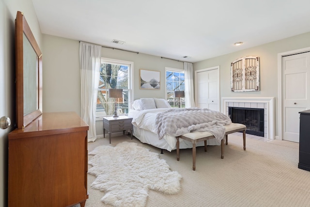 bedroom featuring light carpet, a tiled fireplace, multiple closets, and baseboards