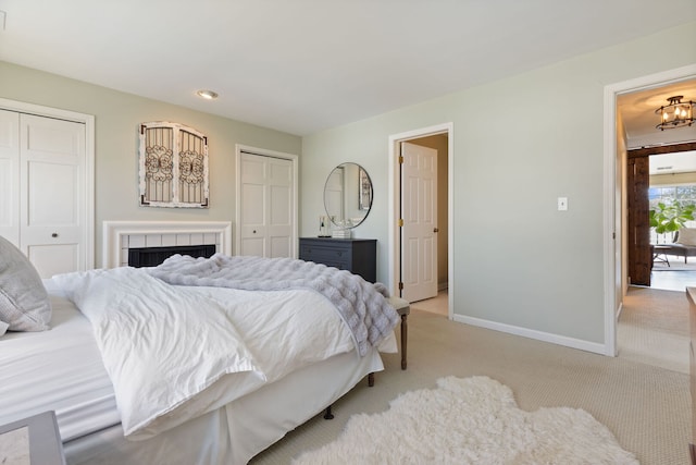 bedroom featuring multiple closets, light colored carpet, baseboards, and a tile fireplace