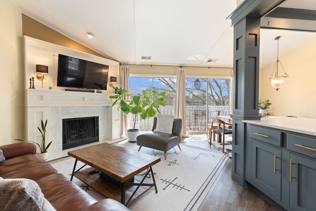 living room featuring lofted ceiling, a high end fireplace, dark wood-type flooring, and a chandelier