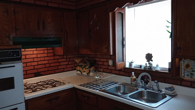 kitchen with oven, a sink, backsplash, range hood, and stovetop