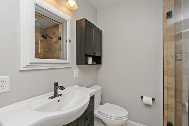 bathroom featuring a tile shower, toilet, vanity, and baseboards