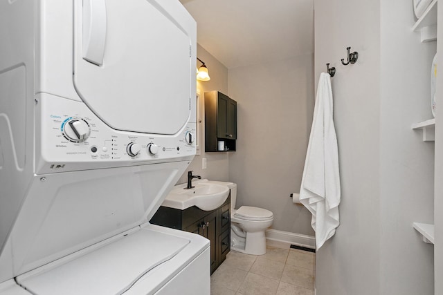 bathroom with stacked washing machine and dryer, baseboards, toilet, tile patterned flooring, and vanity