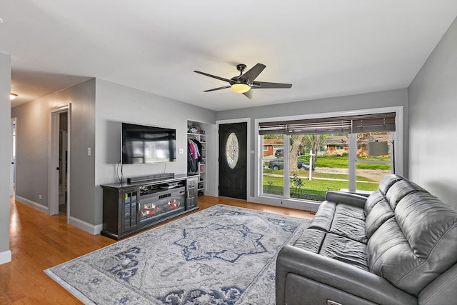 living area with a ceiling fan, baseboards, wood finished floors, and a glass covered fireplace