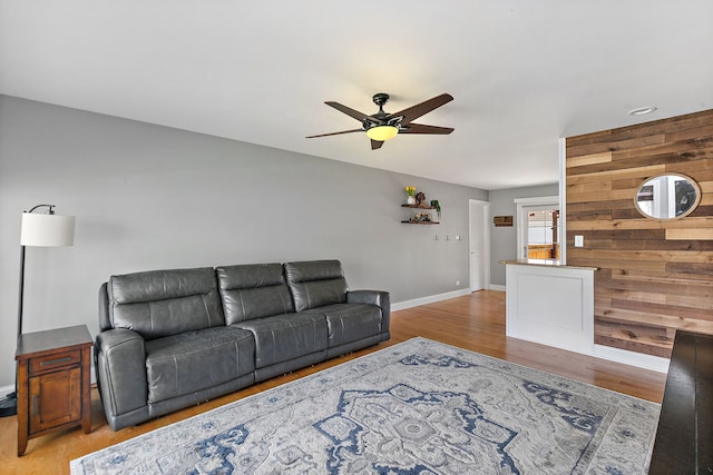 living room with wood finished floors, a ceiling fan, baseboards, and wooden walls