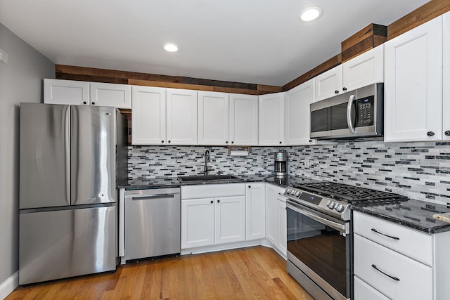 kitchen featuring stainless steel appliances, a sink, light wood-style floors, white cabinetry, and tasteful backsplash