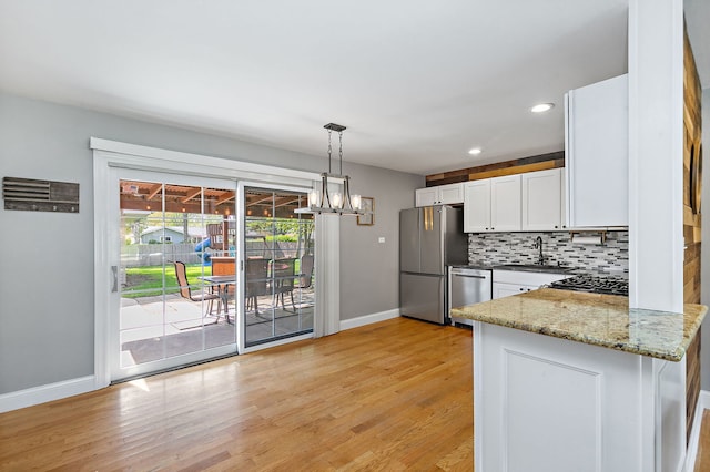 kitchen with appliances with stainless steel finishes, a sink, baseboards, white cabinetry, and backsplash