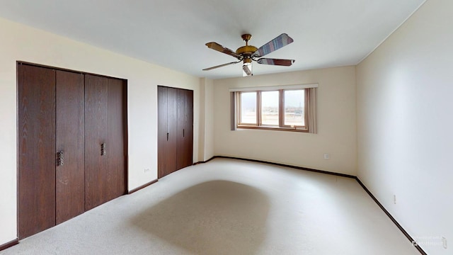 unfurnished bedroom with two closets, baseboards, and a ceiling fan