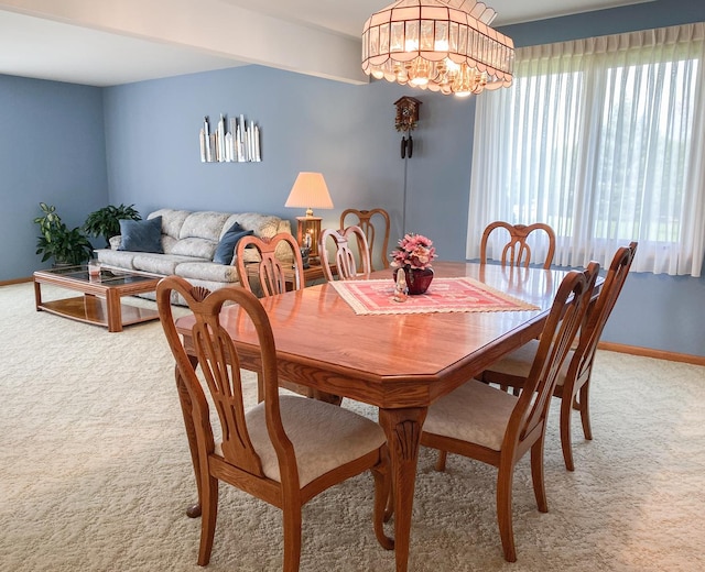 dining room featuring light colored carpet, baseboards, a healthy amount of sunlight, and a chandelier
