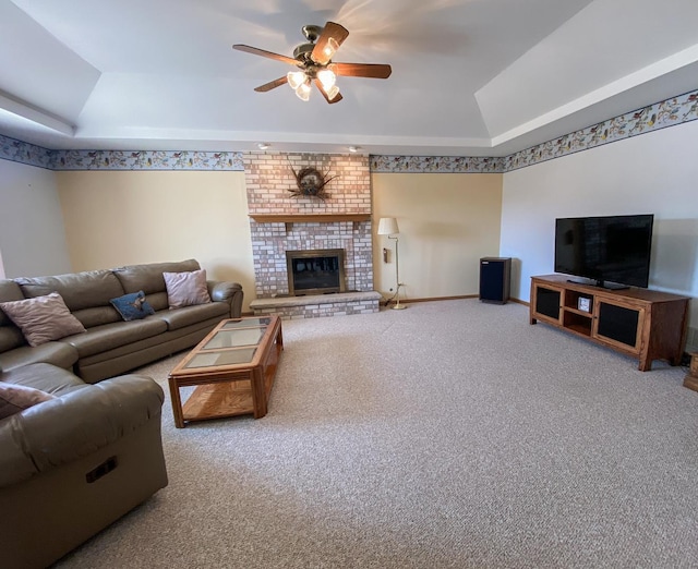 carpeted living area with baseboards, a ceiling fan, a tray ceiling, and a brick fireplace