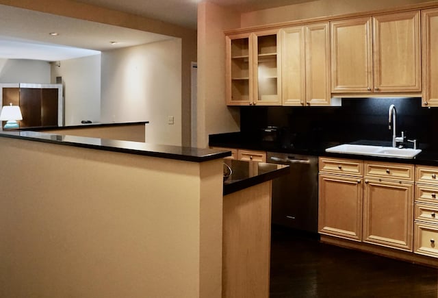kitchen with dark wood-style floors, dark countertops, stainless steel dishwasher, a sink, and glass insert cabinets