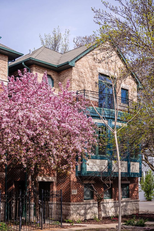 view of front of property featuring fence, brick siding, and a balcony