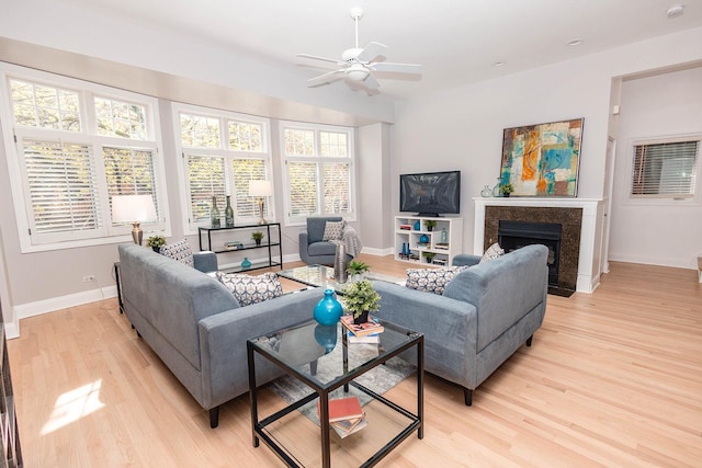 living room with baseboards, a high end fireplace, light wood-type flooring, and a ceiling fan