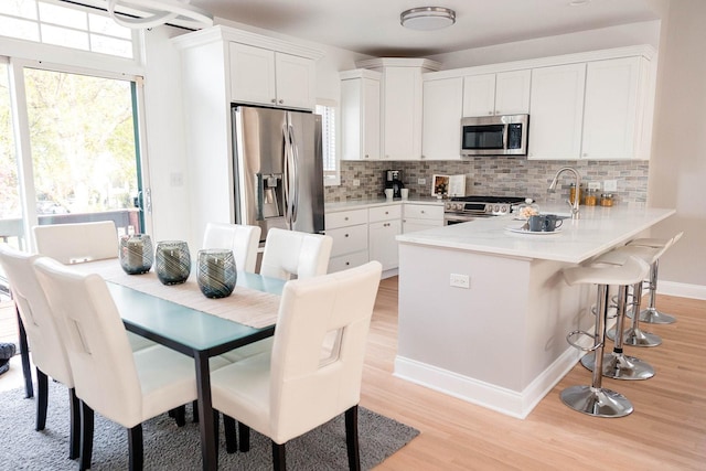 kitchen with a peninsula, stainless steel appliances, white cabinetry, and decorative backsplash