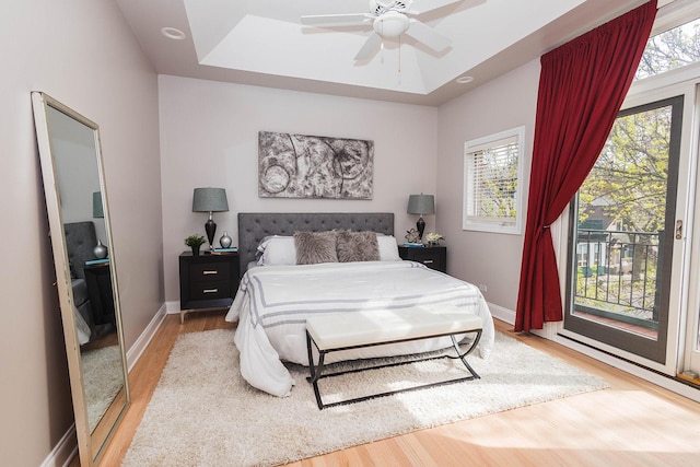 bedroom with multiple windows, access to outside, wood finished floors, and baseboards