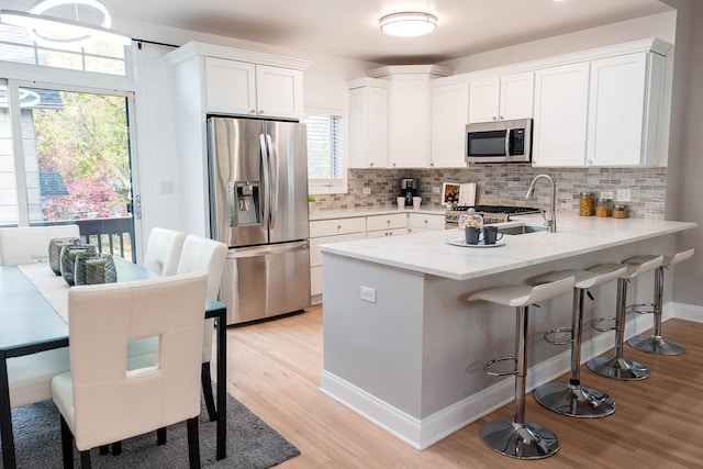 kitchen featuring a peninsula, tasteful backsplash, appliances with stainless steel finishes, white cabinetry, and light wood-style floors