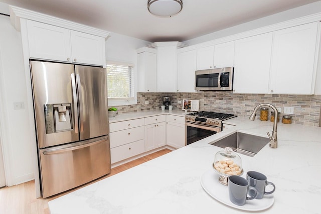 kitchen with a sink, stainless steel appliances, backsplash, light stone countertops, and light wood-style floors