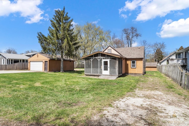 back of property with a sunroom, an outdoor structure, a yard, a fenced backyard, and driveway