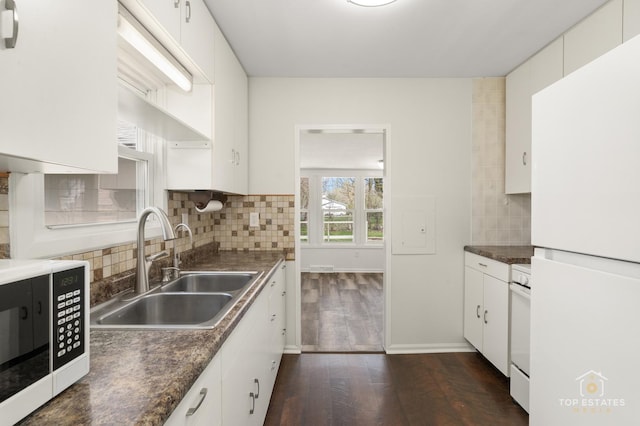 kitchen with a sink, white appliances, dark countertops, white cabinets, and dark wood finished floors